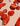 Several bright red hot peppers, some whole and some sliced open to reveal seeds, are arranged on a light-colored surface. The peppers have a wrinkled, glossy texture.