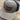 The Black/Grey Puckerbutt Snapback Hat features the embroidered PuckerButt Pepper Company logo above a red and green chili pepper graphic, with the slogan "Pure. Creating. Heat." below, all displayed on a wooden surface.