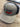 The Black/Grey Puckerbutt Snapback Hat features the embroidered PuckerButt Pepper Company logo above a red and green chili pepper graphic, with the slogan "Pure. Creating. Heat." below, all displayed on a wooden surface.