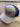 The Blue/Grey Puckerbutt Snapback Hat, featuring an embroidered PuckerButt Pepper Company logo with a chili pepper design, rests on a wood-textured surface.